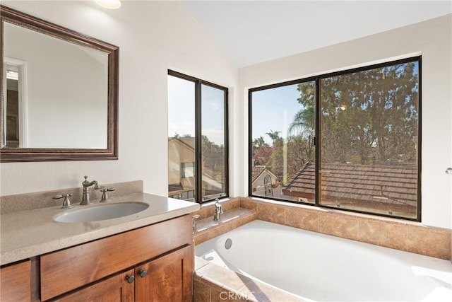 bathroom featuring tiled bath, vanity, and vaulted ceiling