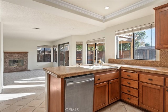 kitchen featuring stainless steel dishwasher, decorative backsplash, a stone fireplace, and kitchen peninsula