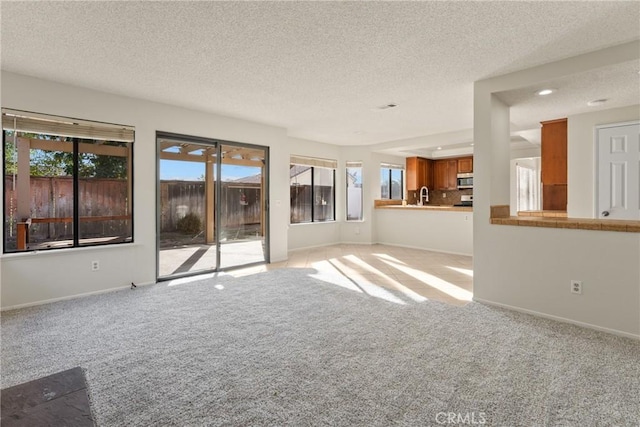 unfurnished living room with light colored carpet, sink, and a textured ceiling