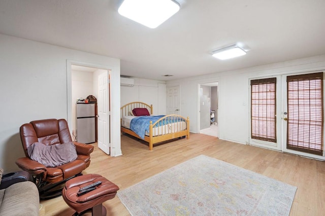 bedroom featuring stainless steel refrigerator, a wall unit AC, ensuite bathroom, wood-type flooring, and access to outside