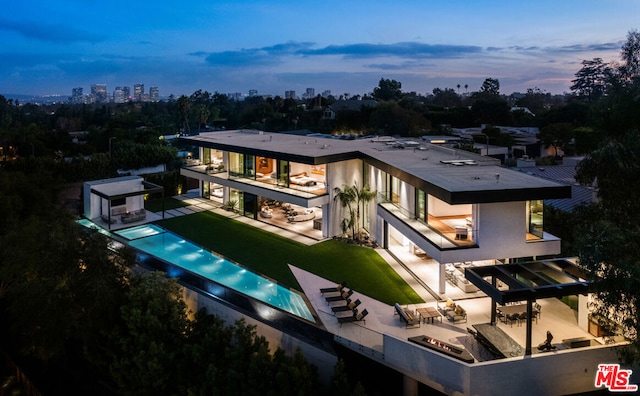 back house at dusk featuring a yard, a patio area, and a swimming pool