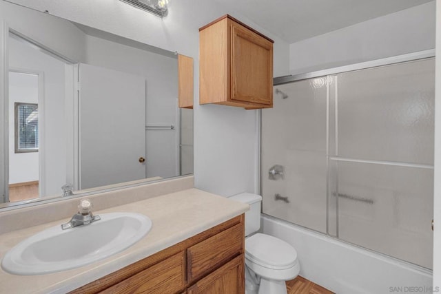 full bathroom with combined bath / shower with glass door, vanity, and toilet