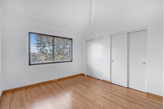 unfurnished bedroom featuring light hardwood / wood-style floors, lofted ceiling with beams, and multiple closets