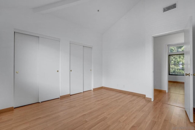 unfurnished bedroom featuring beam ceiling, multiple closets, high vaulted ceiling, and light hardwood / wood-style floors