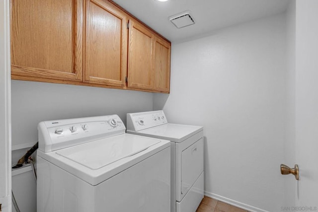 clothes washing area featuring washer and clothes dryer, light tile patterned flooring, and cabinets