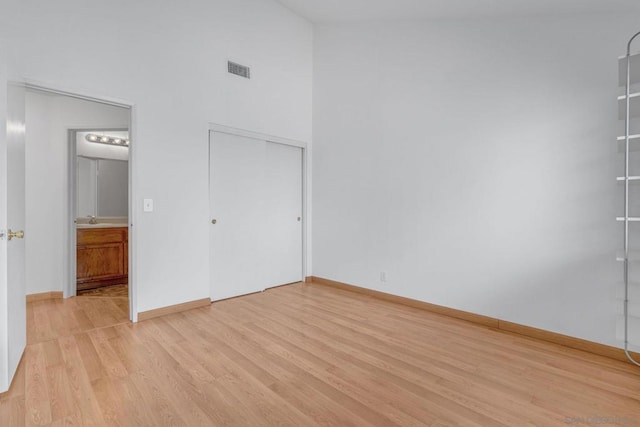 unfurnished bedroom featuring a closet, a towering ceiling, sink, and light hardwood / wood-style flooring