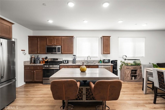 kitchen featuring appliances with stainless steel finishes, light wood-type flooring, a kitchen island, a breakfast bar, and sink