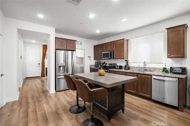 kitchen featuring appliances with stainless steel finishes, light hardwood / wood-style floors, washer / clothes dryer, and sink