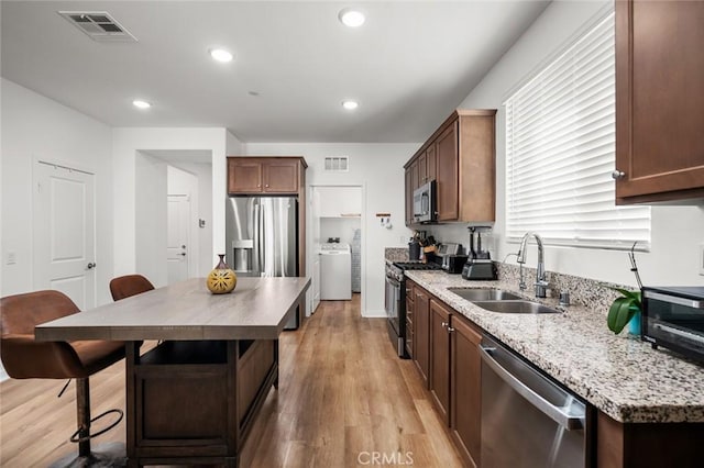 kitchen featuring washer / dryer, stainless steel appliances, light hardwood / wood-style floors, sink, and a breakfast bar