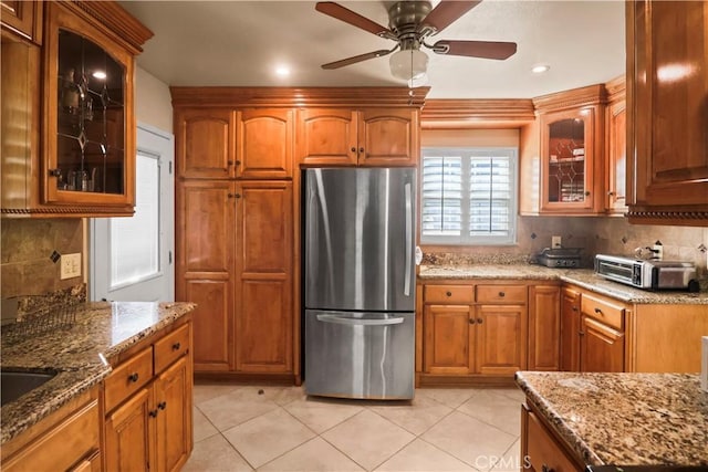 kitchen with ceiling fan, decorative backsplash, light stone counters, and stainless steel refrigerator