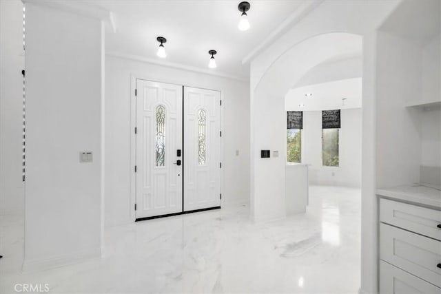 entrance foyer featuring marble finish floor, arched walkways, and crown molding