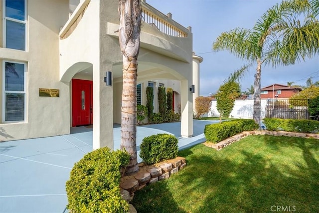 entrance to property featuring a lawn, fence, and stucco siding