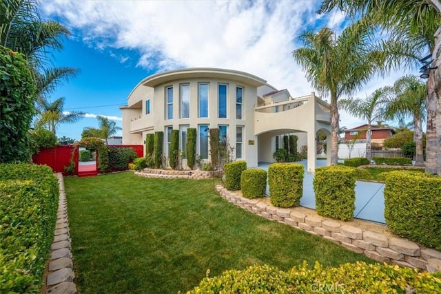 rear view of house featuring a yard, fence, a balcony, and stucco siding