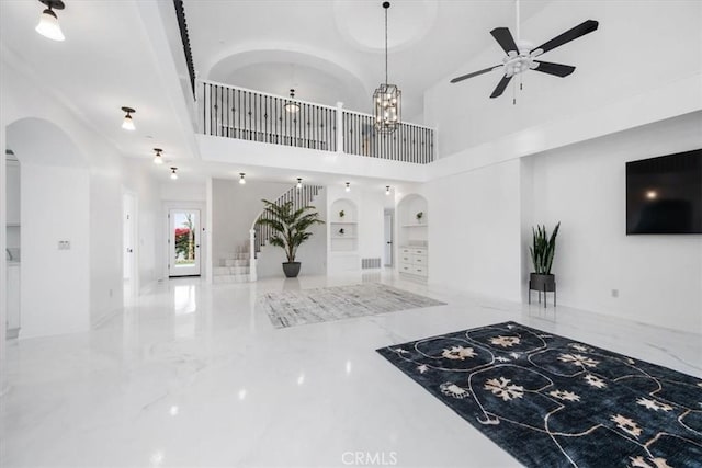 interior space with ceiling fan with notable chandelier, built in features, a high ceiling, and decorative light fixtures