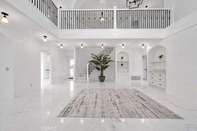 interior space featuring built in shelves, a towering ceiling, visible vents, marble finish floor, and stairway