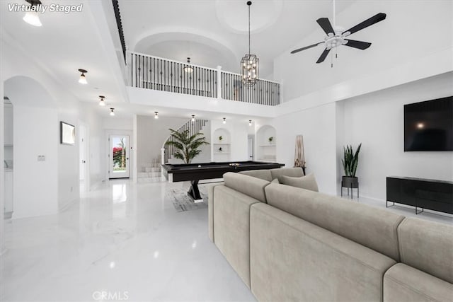 living area featuring arched walkways, marble finish floor, pool table, stairway, and a high ceiling