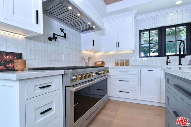 kitchen with backsplash, light hardwood / wood-style floors, custom range hood, high end stainless steel range, and white cabinets