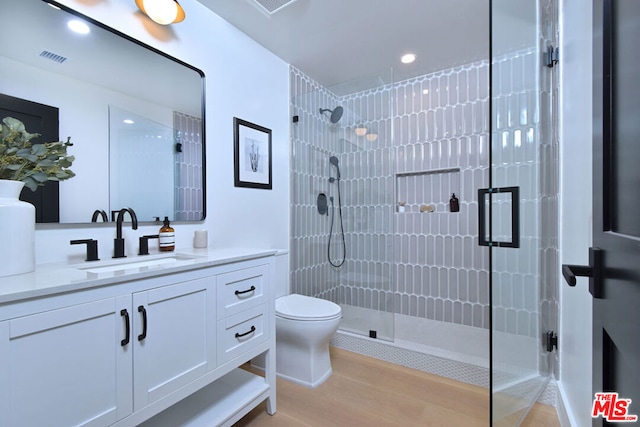 bathroom featuring hardwood / wood-style flooring, toilet, vanity, and a shower with door