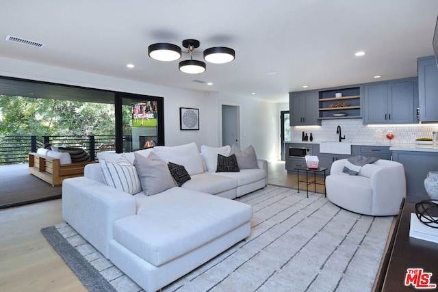 living room featuring ceiling fan, sink, and light wood-type flooring