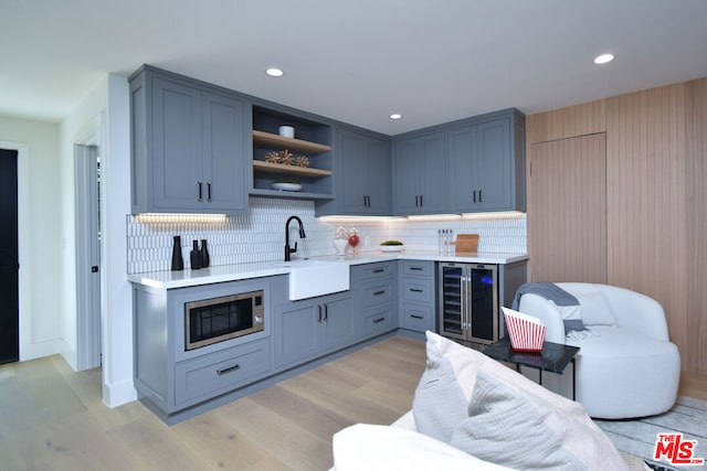 kitchen featuring stainless steel microwave, decorative backsplash, wine cooler, light hardwood / wood-style flooring, and sink