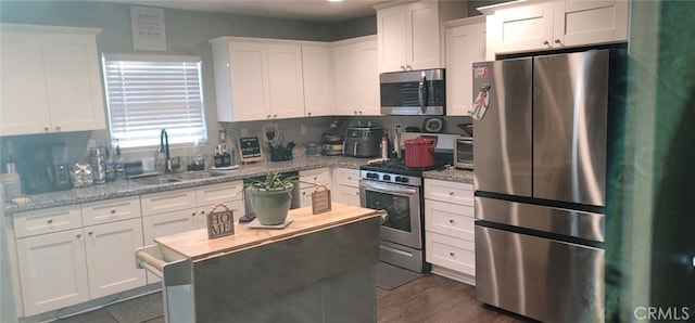 kitchen with stainless steel appliances, light stone countertops, sink, and white cabinets