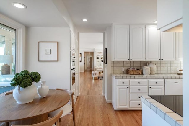 kitchen with tile countertops, white cabinetry, light hardwood / wood-style floors, tasteful backsplash, and white dishwasher