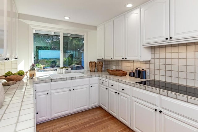 kitchen featuring white cabinetry, light wood-type flooring, tile countertops, and tasteful backsplash