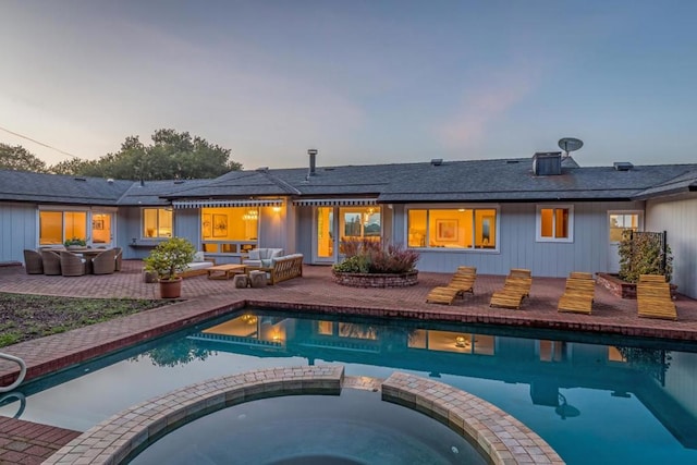 back house at dusk with outdoor lounge area, a pool with hot tub, and a patio