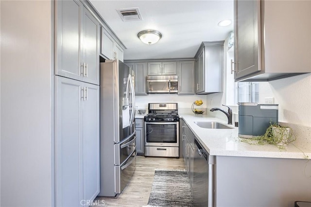 kitchen with sink, light wood-type flooring, appliances with stainless steel finishes, gray cabinetry, and light stone counters