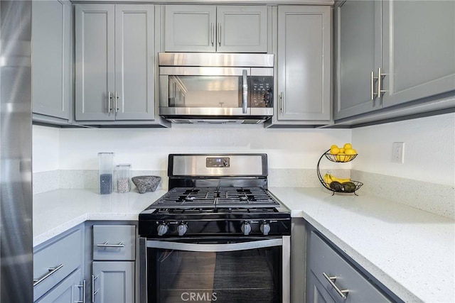 kitchen featuring appliances with stainless steel finishes, gray cabinetry, and light stone counters