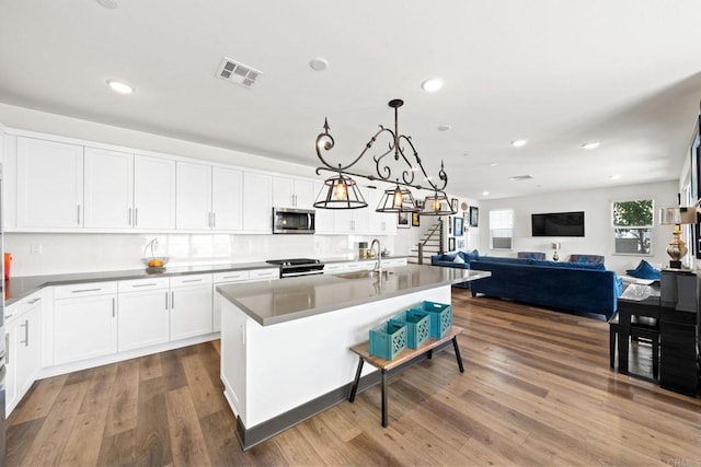 kitchen featuring dark wood-type flooring, hanging light fixtures, stainless steel appliances, a kitchen island with sink, and white cabinets