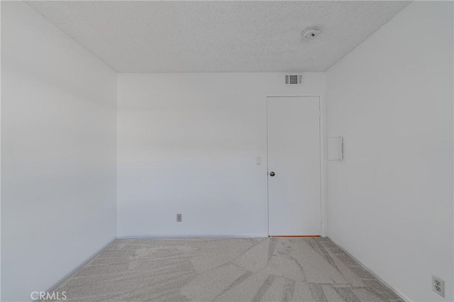 unfurnished room with baseboards, visible vents, a textured ceiling, and light colored carpet