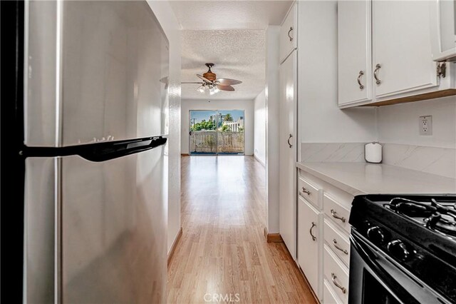 kitchen featuring range with gas stovetop, light countertops, freestanding refrigerator, white cabinets, and light wood-style floors
