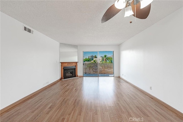 unfurnished living room featuring a textured ceiling, a ceiling fan, a fireplace with flush hearth, visible vents, and light wood finished floors