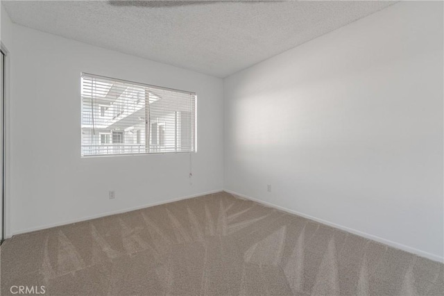 carpeted spare room with a textured ceiling and baseboards
