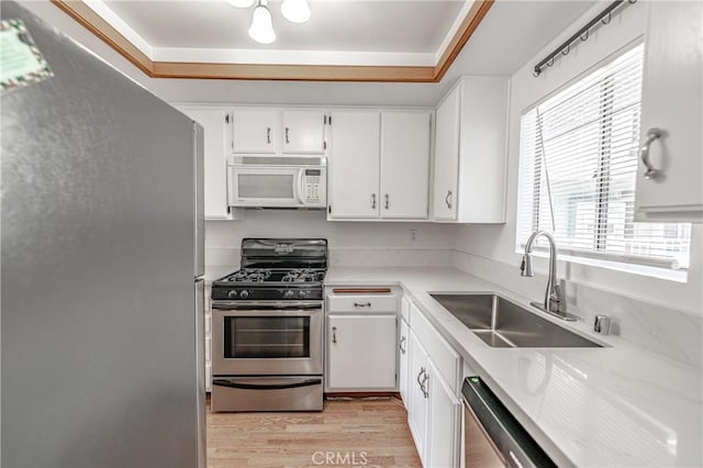 kitchen featuring appliances with stainless steel finishes, a raised ceiling, white cabinets, light hardwood / wood-style flooring, and sink