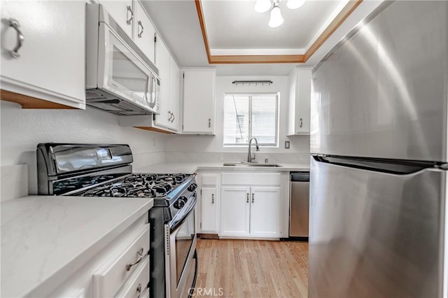 kitchen with white cabinets, stainless steel appliances, sink, a raised ceiling, and light wood-type flooring