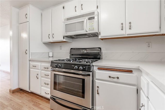 kitchen featuring stainless steel range with gas stovetop, light countertops, light wood-type flooring, white microwave, and white cabinetry