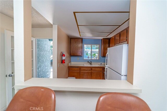 kitchen with sink, a textured ceiling, white refrigerator, and kitchen peninsula