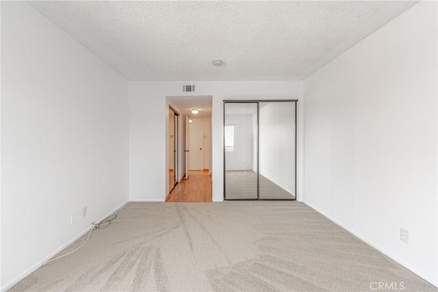 unfurnished bedroom with baseboards, a closet, a textured ceiling, visible vents, and carpet