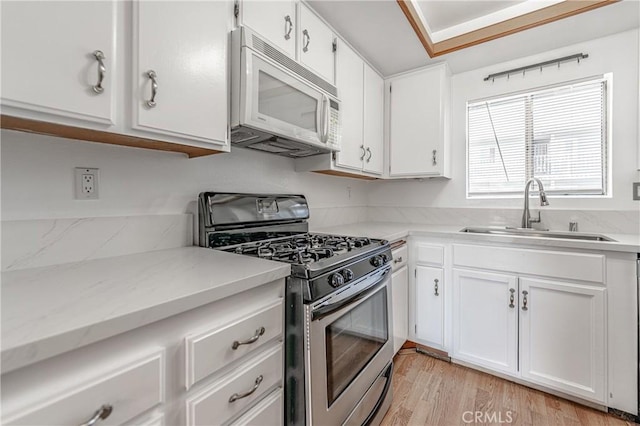 kitchen with white microwave, white cabinetry, stainless steel range with gas cooktop, light stone countertops, and a sink