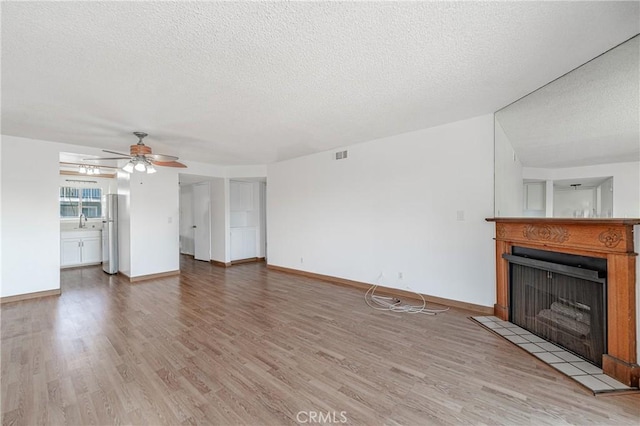 unfurnished living room featuring a fireplace, a textured ceiling, a ceiling fan, visible vents, and wood finished floors