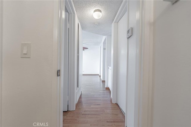 hall with light wood finished floors and a textured ceiling
