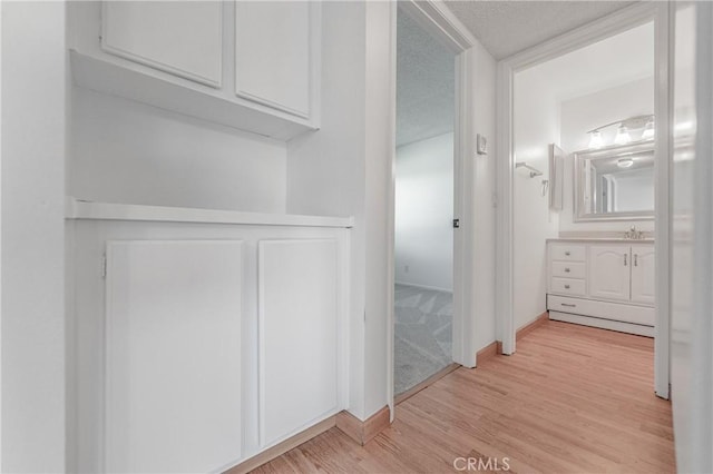 hall with a textured ceiling, light hardwood / wood-style flooring, and sink