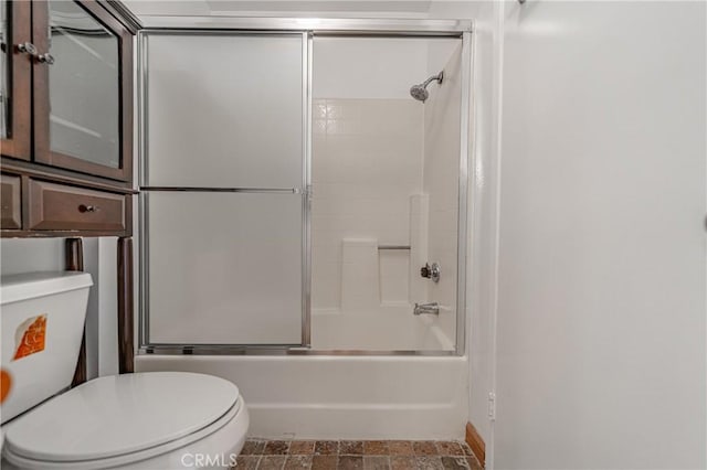 full bathroom featuring stone finish flooring, bath / shower combo with glass door, and toilet