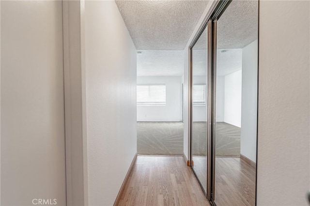 corridor featuring baseboards, a textured ceiling, and wood finished floors