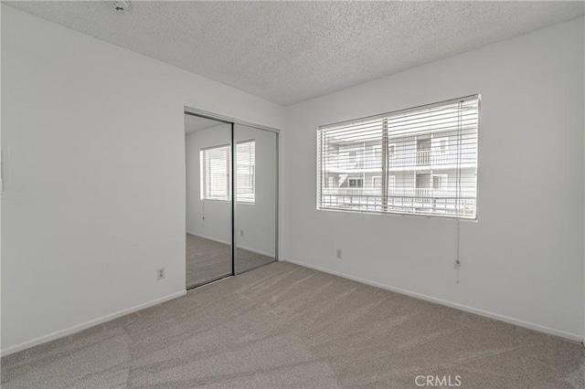 unfurnished bedroom featuring light colored carpet, a textured ceiling, and a closet