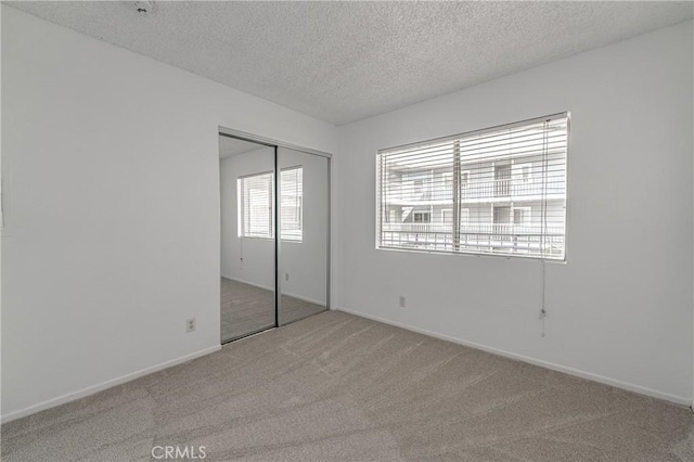 unfurnished bedroom with a closet, carpet, a textured ceiling, and baseboards