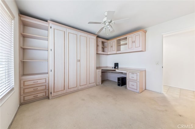 unfurnished office featuring ceiling fan, light colored carpet, and built in desk