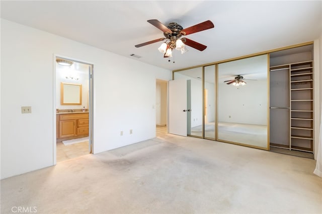 unfurnished bedroom with ensuite bath, light colored carpet, ceiling fan, and a closet